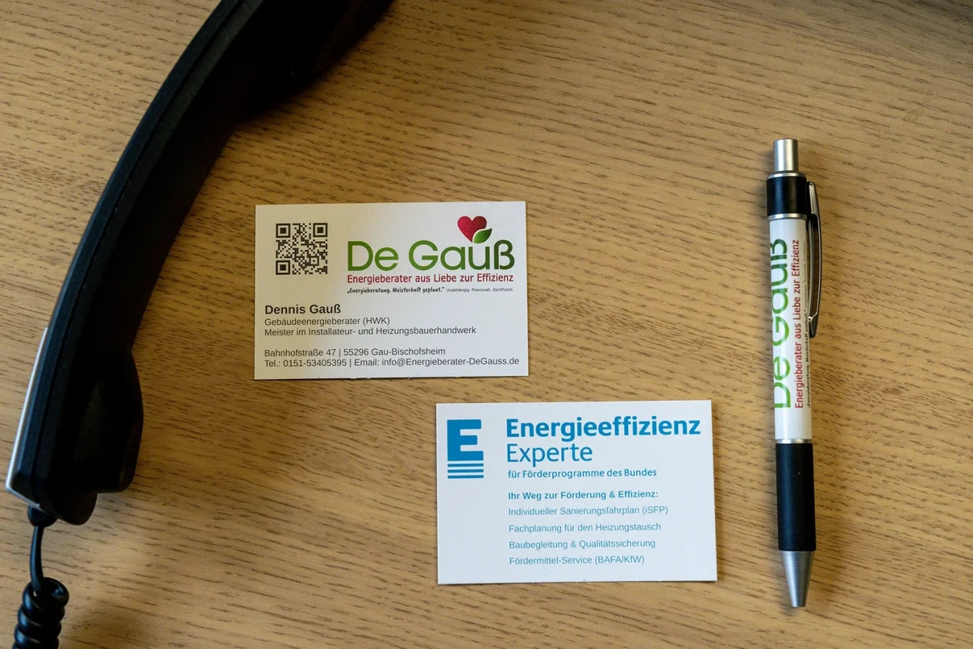 Visitenkarte von Dennis Gauß (Energieberater De Gauß) neben einem Zollstock und einem Stift auf einem Holztisch – Symbol für die Kooperation