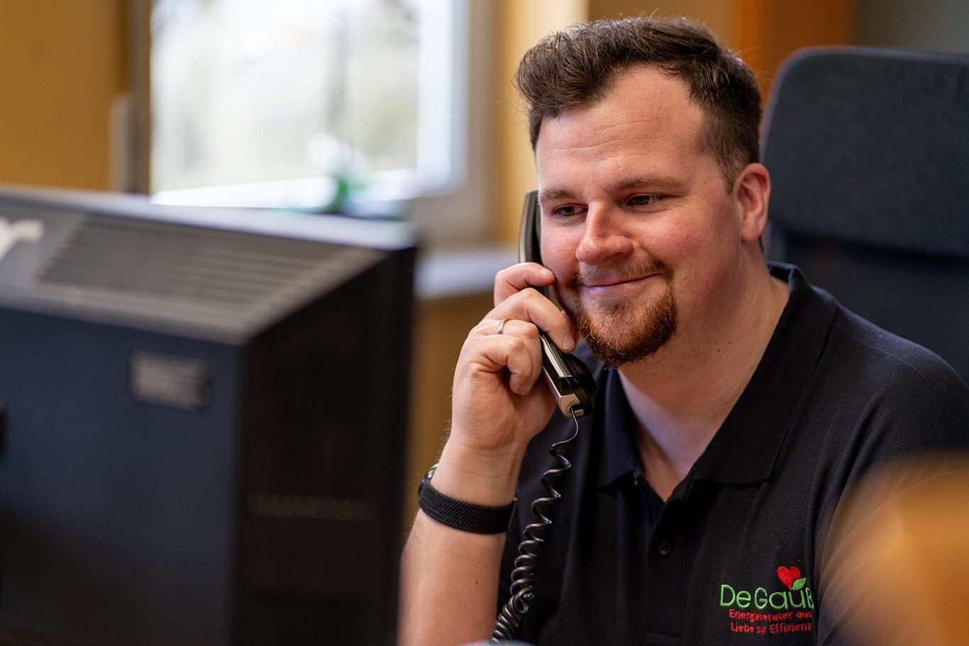 Dennis Gauß von Energieberater De Gauß in Mainz lächelt am Telefon im Büro – bereit für die Beratung nach einer Online-Terminbuchung.